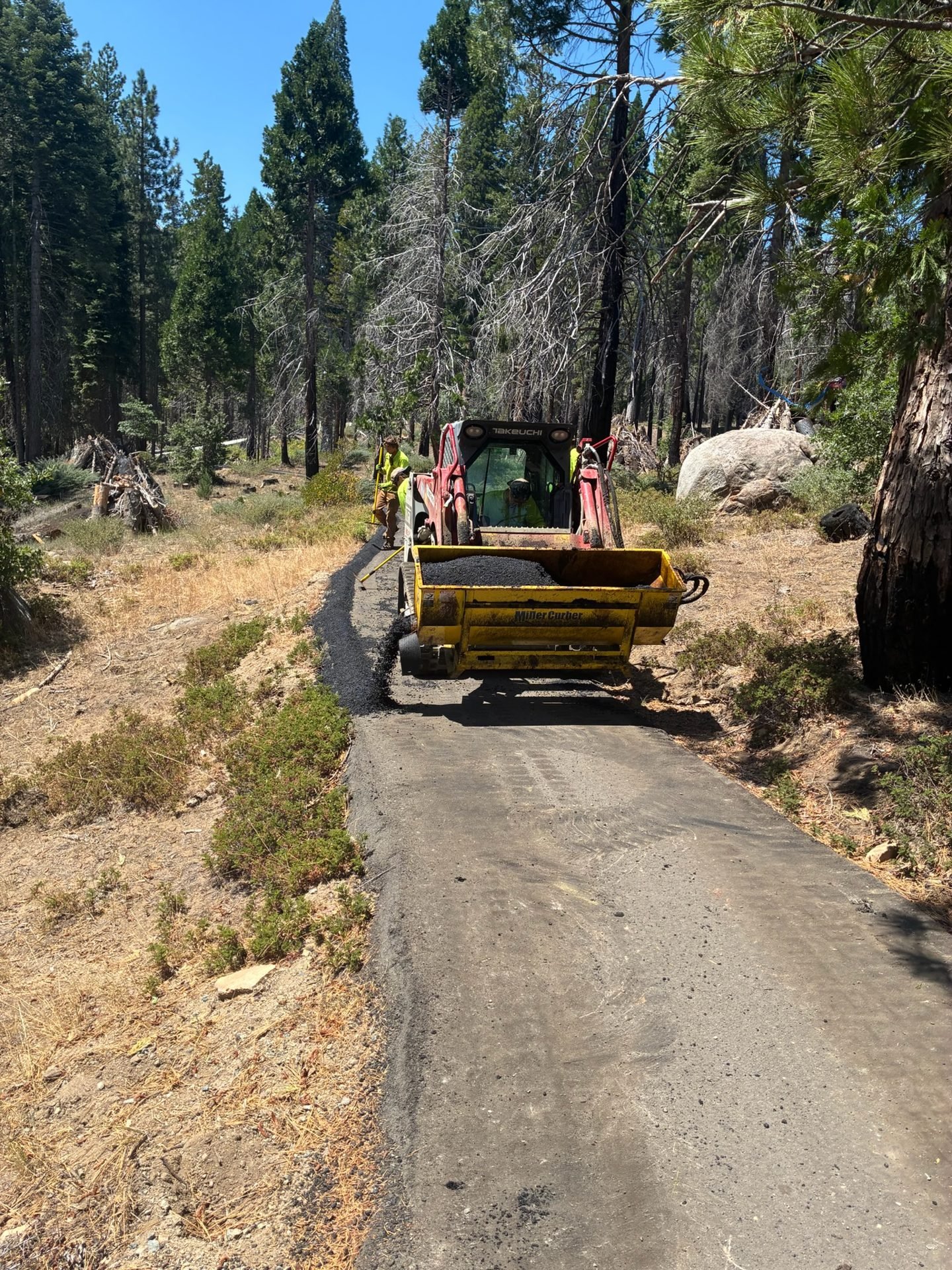 Skid steer with asphalt curber building the trail berm on the Bush Loop project