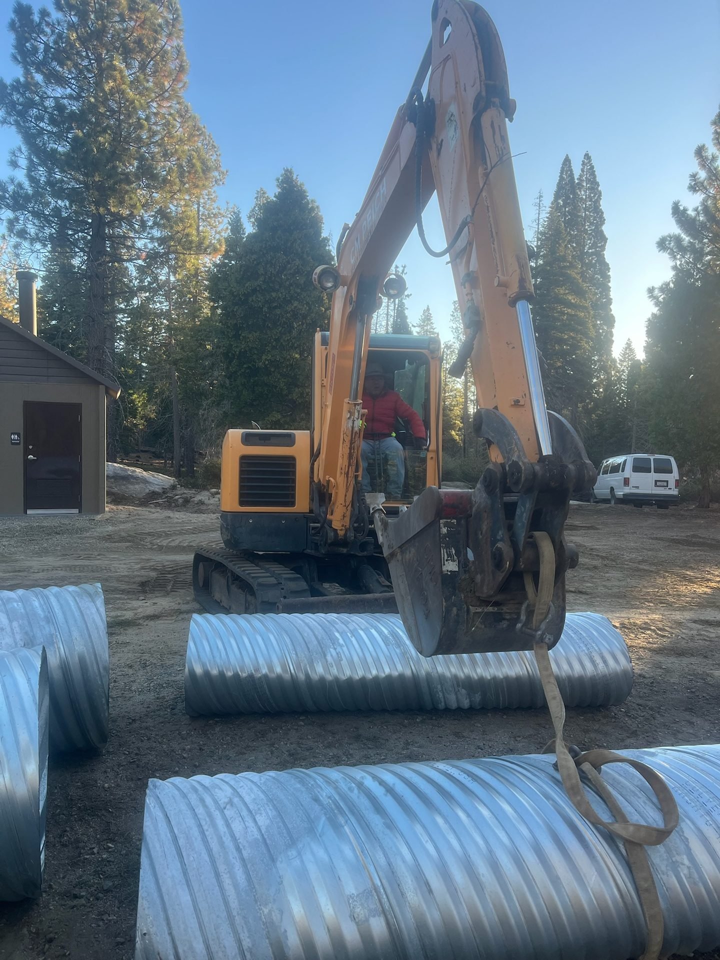 Excavator staging corrugated metal culvert pipe at a forest recreation site