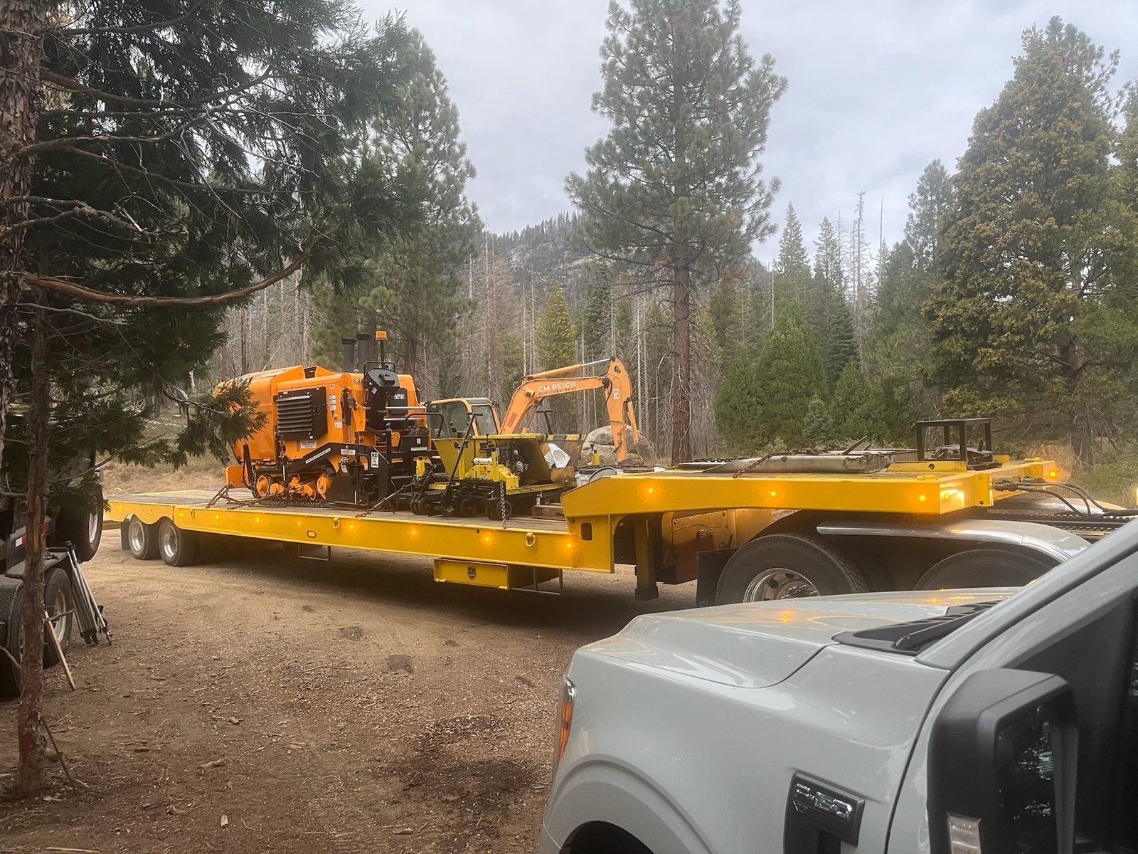 Paver and excavator mobilized on a lowboy trailer to a remote mountain jobsite