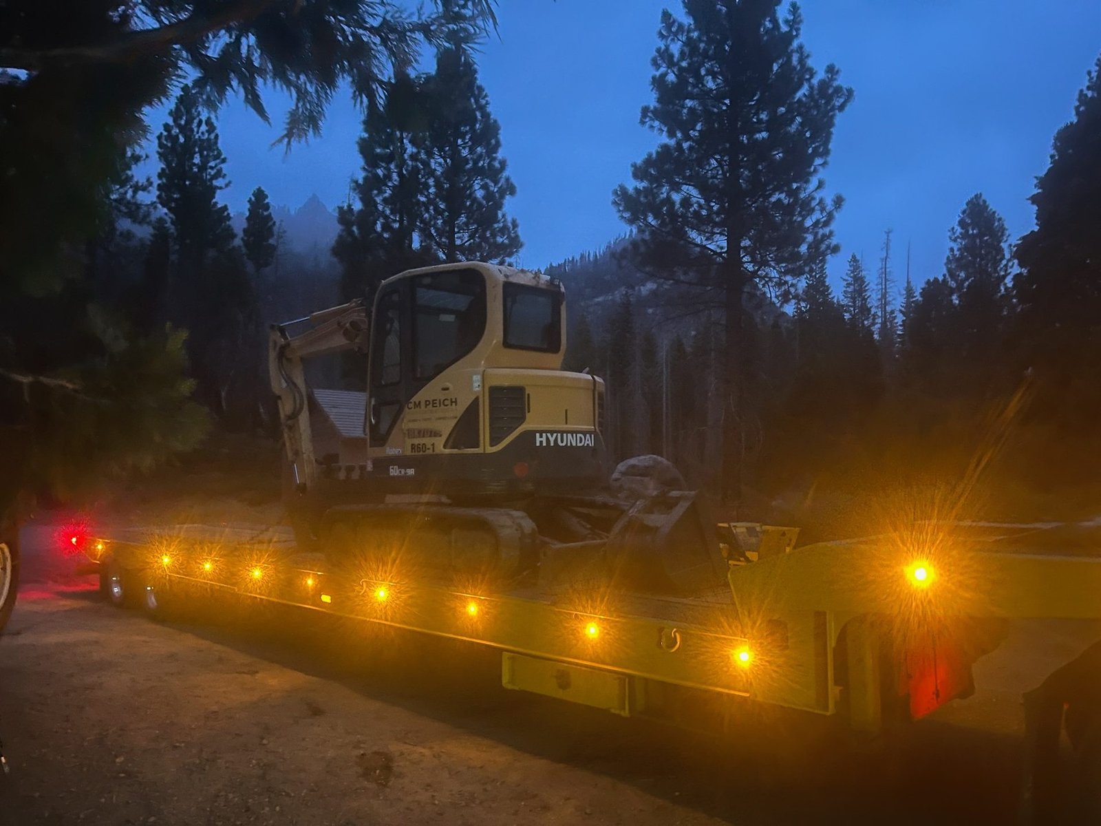 Excavator loaded on a lowboy trailer at dusk in the Sierra Nevada
